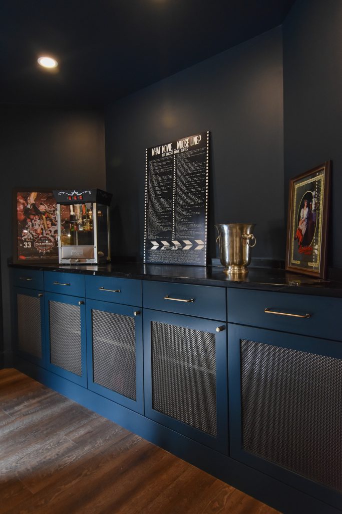 Basement game room storage wall with blue cabinetry, mesh cabinet fronts, and a popcorn machine on a black counter
