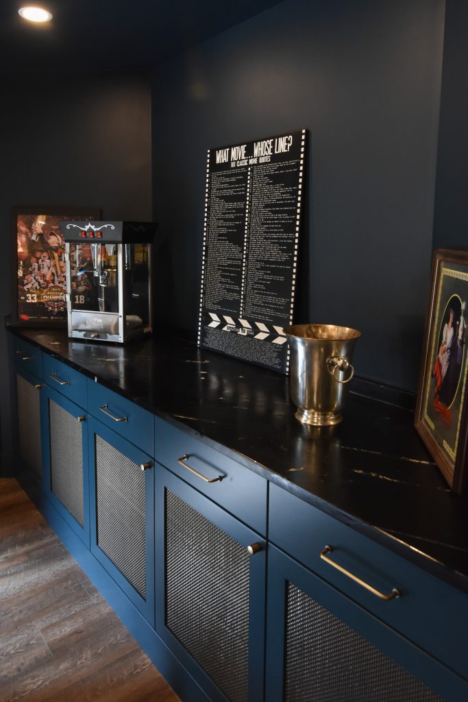 Blue mesh-front built-in cabinetry and black stone counter in a basement game and media room