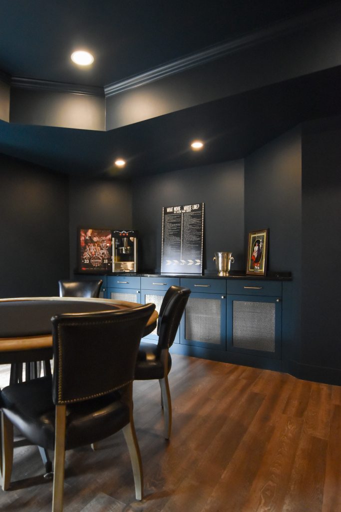 Basement game room with a poker table and custom blue cabinetry with metal mesh door panels