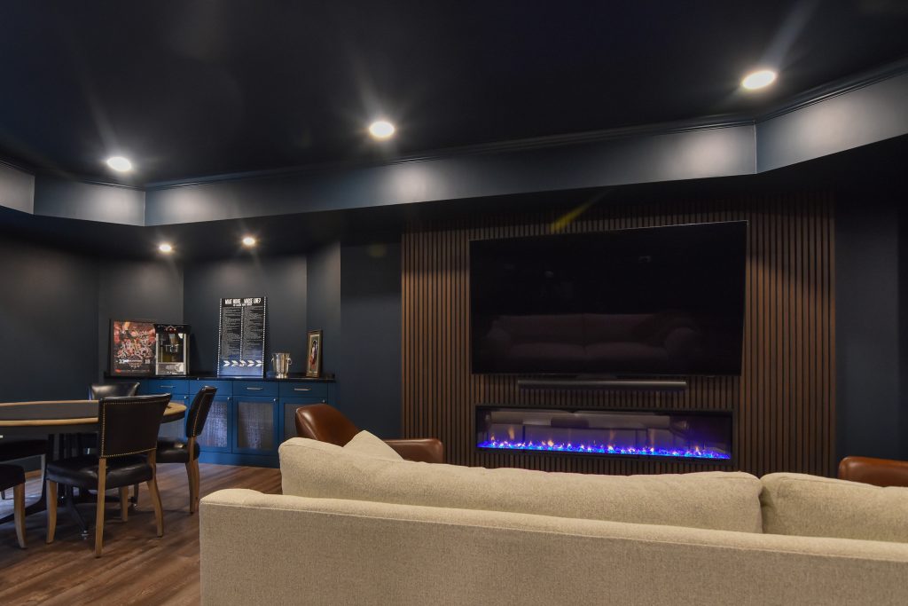 Basement entertainment area with a linear fireplace, mounted TV, and adjoining game table space