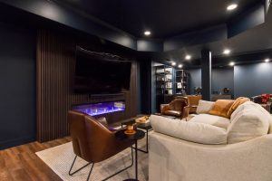 Finished basement living area with a fireplace media wall, leather chairs, and a home office beyond