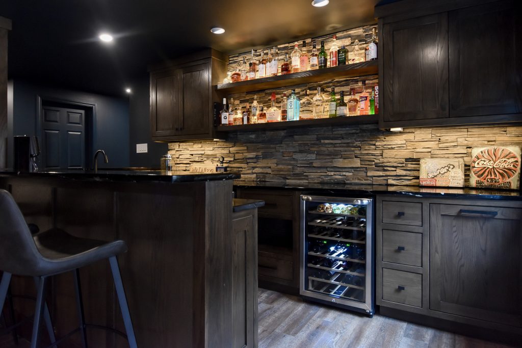 Basement bar with backlit liquor shelving, stacked stone backsplash, and a built-in glass-front wine refrigerator