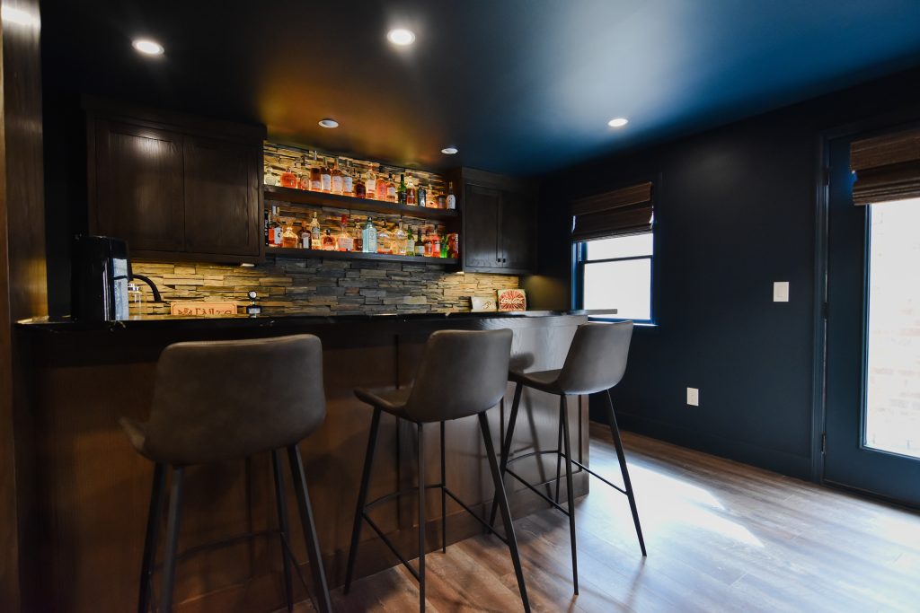 Basement wet bar seating with three leather stools and a black stone countertop beneath a window