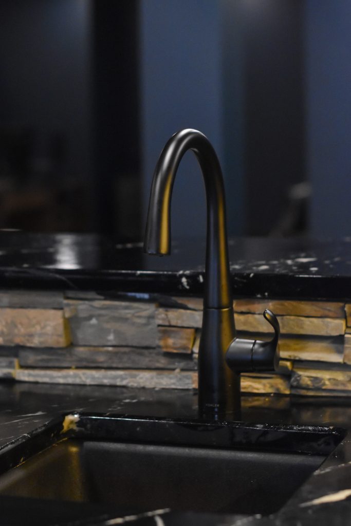 Matte black bar faucet over an undermount sink set in a black stone countertop