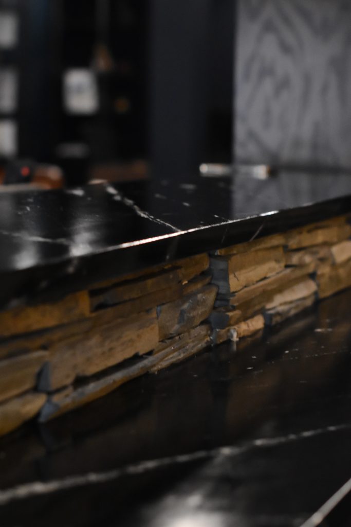 Black stone bar countertop with gold veining meeting a stacked stone backsplash