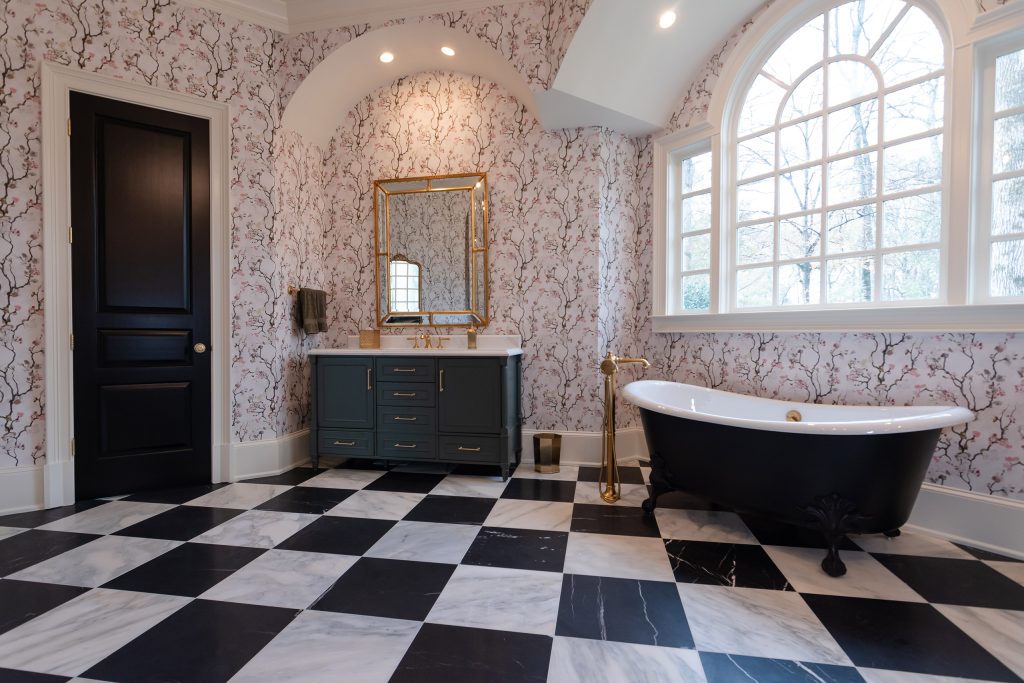 Wide bath with charcoal vanity, black paneled door, and black clawfoot tub under an arched window on marble checkerboard.