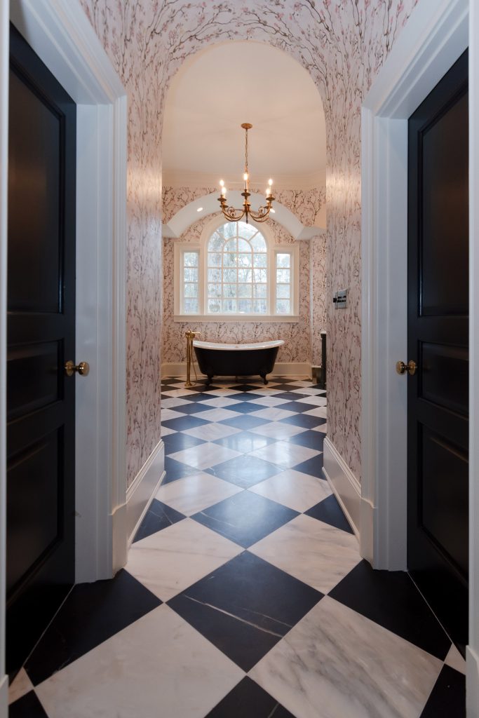 Hallway flanked by black paneled doors opening to a black clawfoot tub under an arched window.
