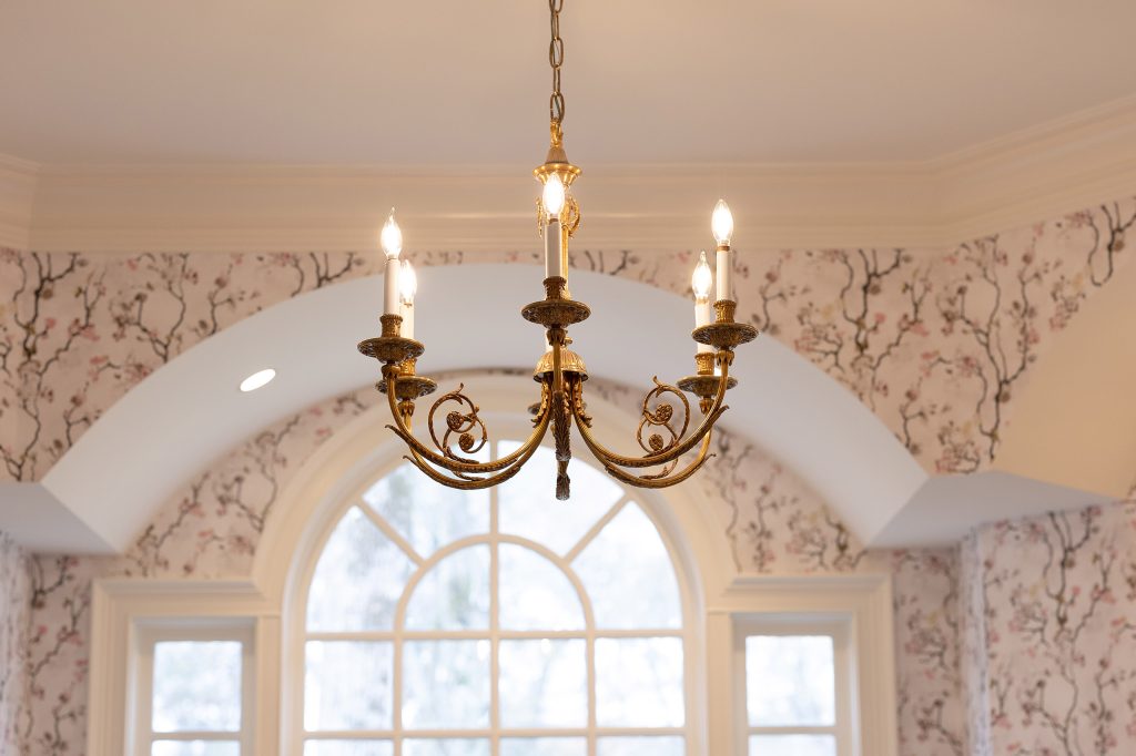 Gilded six-arm candle chandelier hanging inside a barrel-vaulted ceiling above an arched divided-light window.