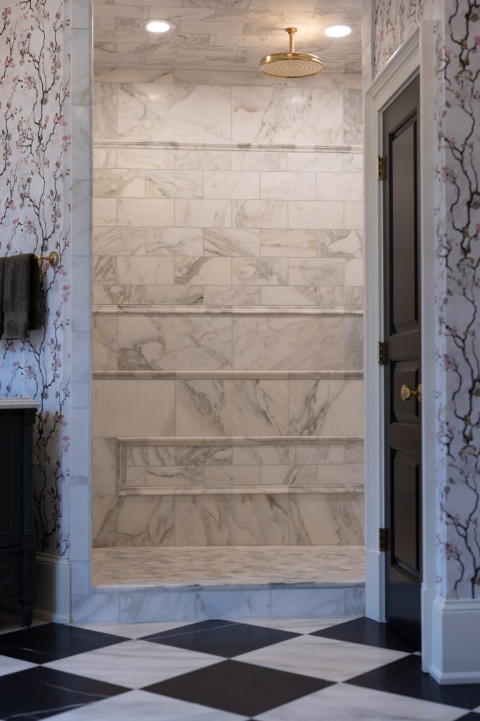 Marble walk-in shower with brushed-gold rain head, framed niche, and hex-tile floor between blossom-print walls.