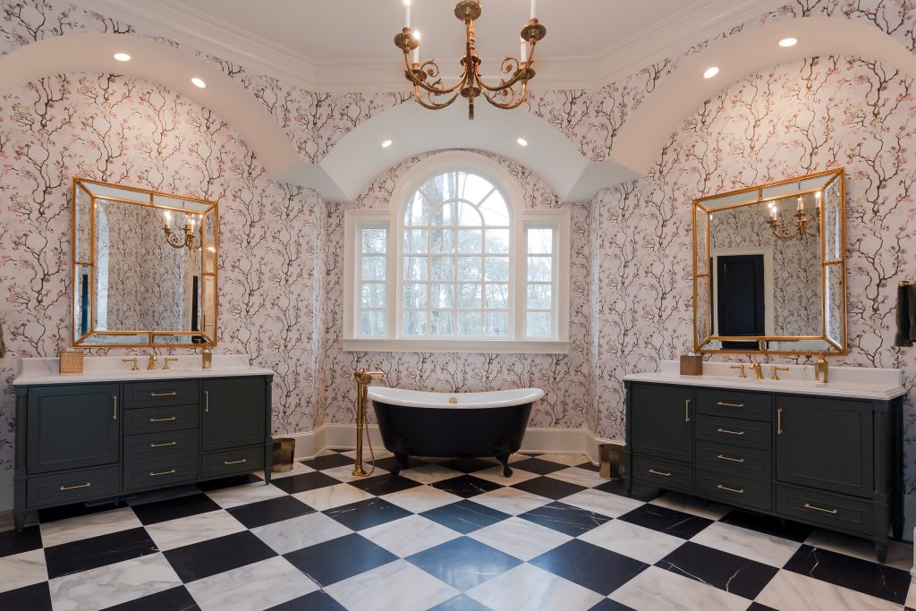 Vaulted bath with two charcoal vanities, gilded chandelier, and a black clawfoot tub under an arched window.