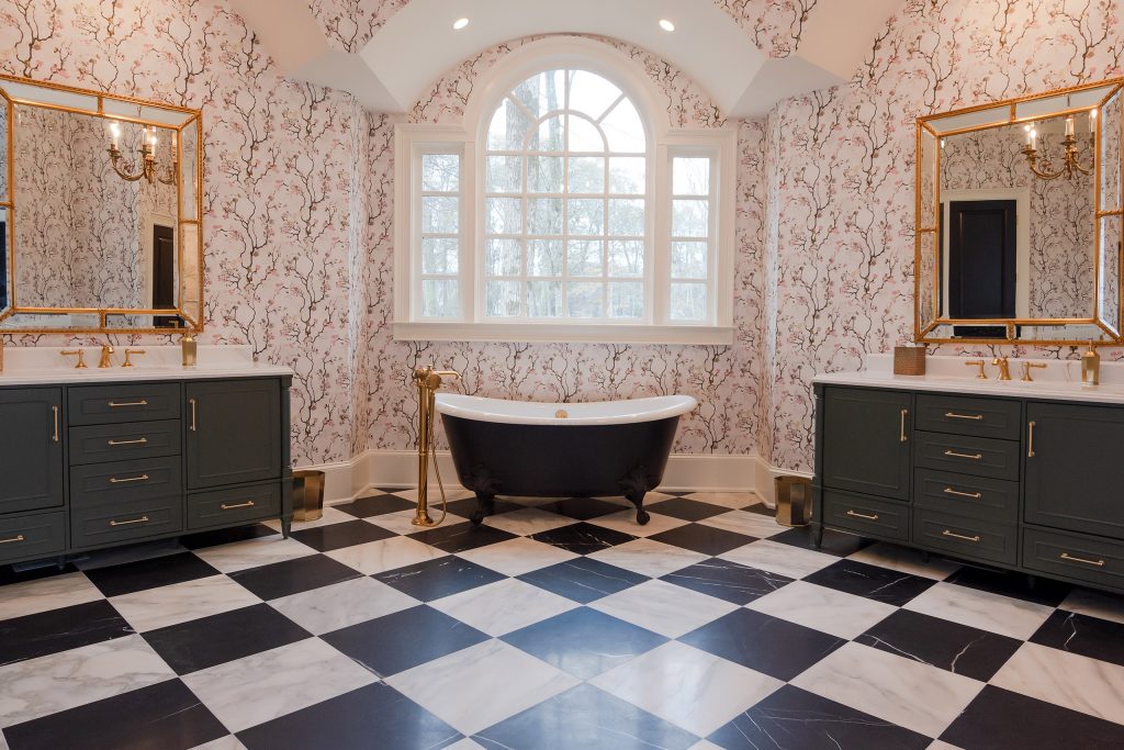 Dual charcoal vanities and gold mirrors surround a black clawfoot tub below an arched window in a blossom-papered bath.