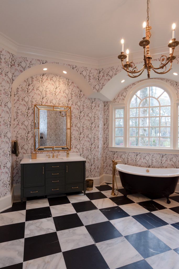View down a vaulted blossom-papered room to a black clawfoot tub under an arched Palladian window.