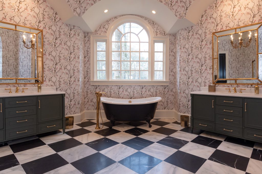 Twin charcoal vanities with gold mirrors flank a black clawfoot tub under an arched window on checkerboard marble.