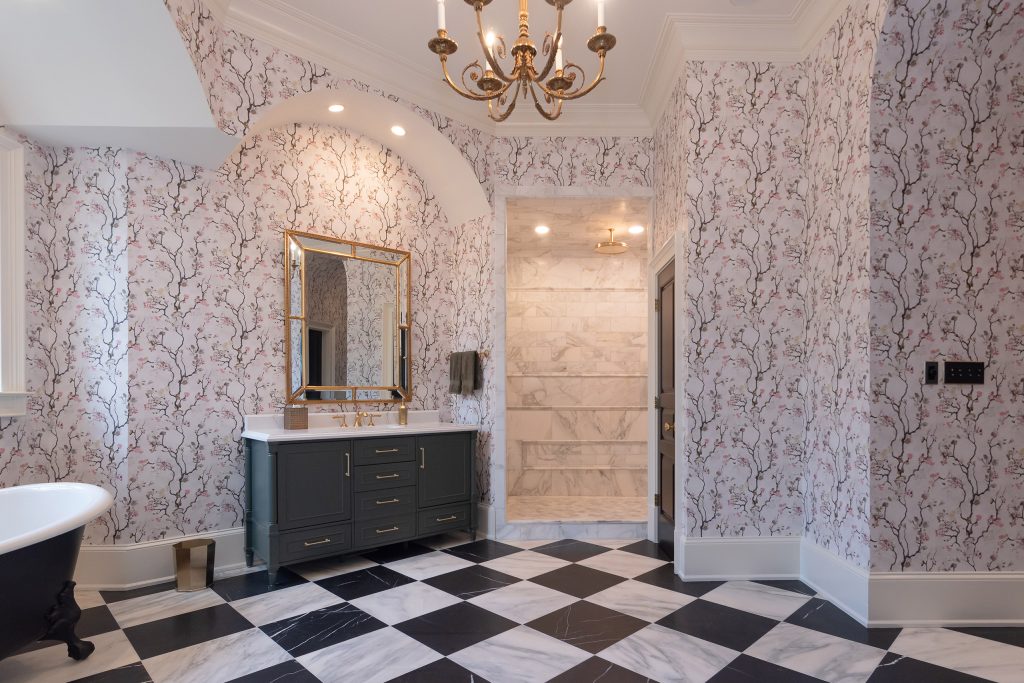 Vaulted blossom-papered bath with charcoal vanity, marble walk-in shower, and edge of a black clawfoot tub.