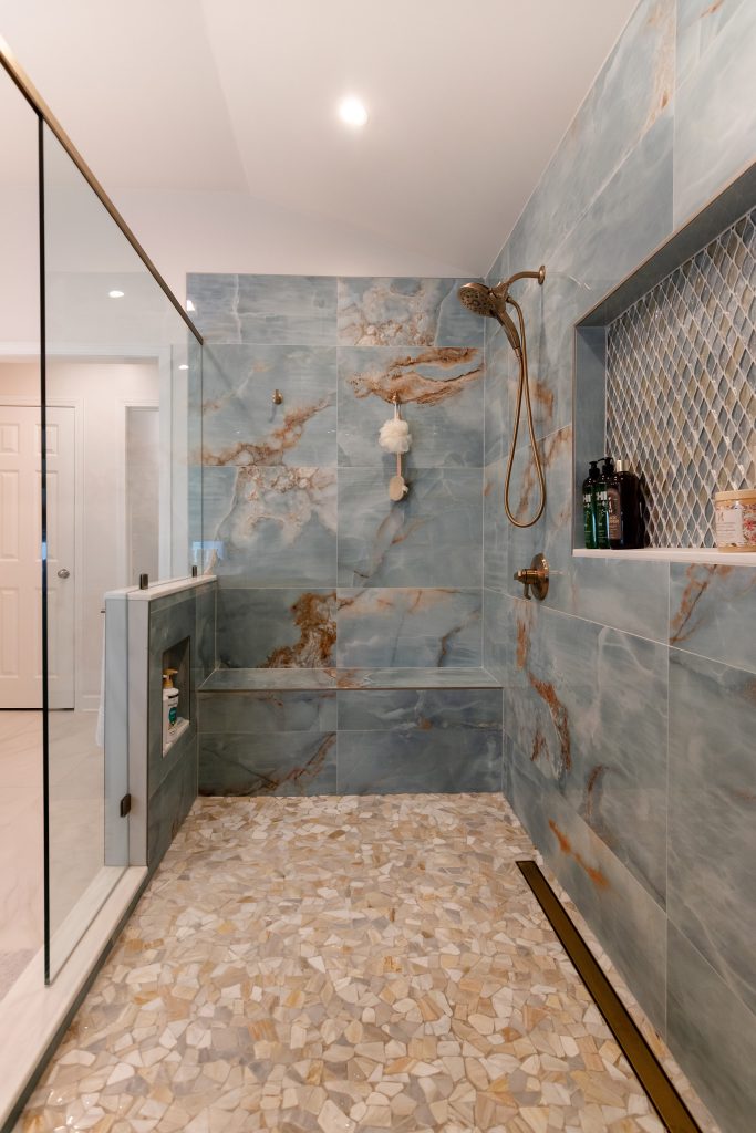 Blue onyx shower with a diamond mosaic niche, a long bench, and pebble floor, glass wall and bathroom door to the left.