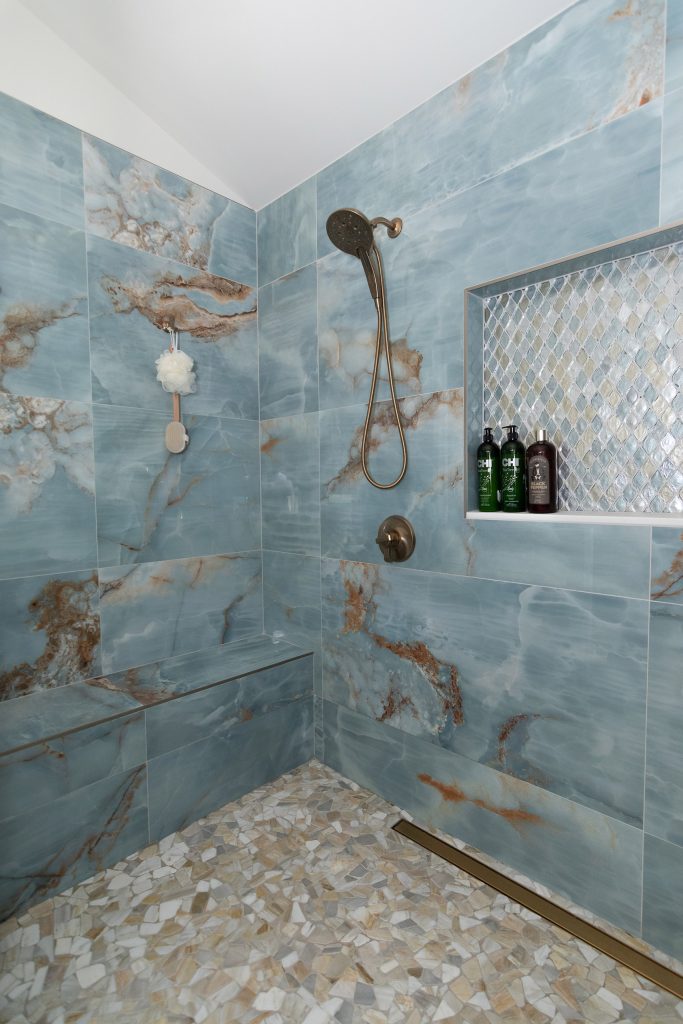 Corner of the blue onyx shower with a diamond mosaic niche, a bench, and pebble floor under a vaulted ceiling.
