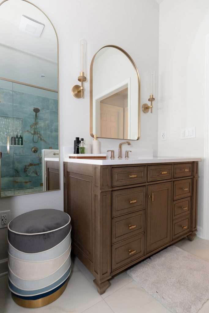 Dark-wood vanity with white quartz, a striped blue ottoman, and arched mirrors reflecting the veined onyx shower.