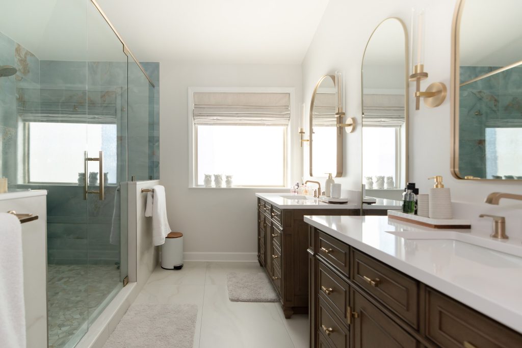 Master bath with a glass onyx shower on the left, a window with roman shade, and dark vanities with white quartz on the right.