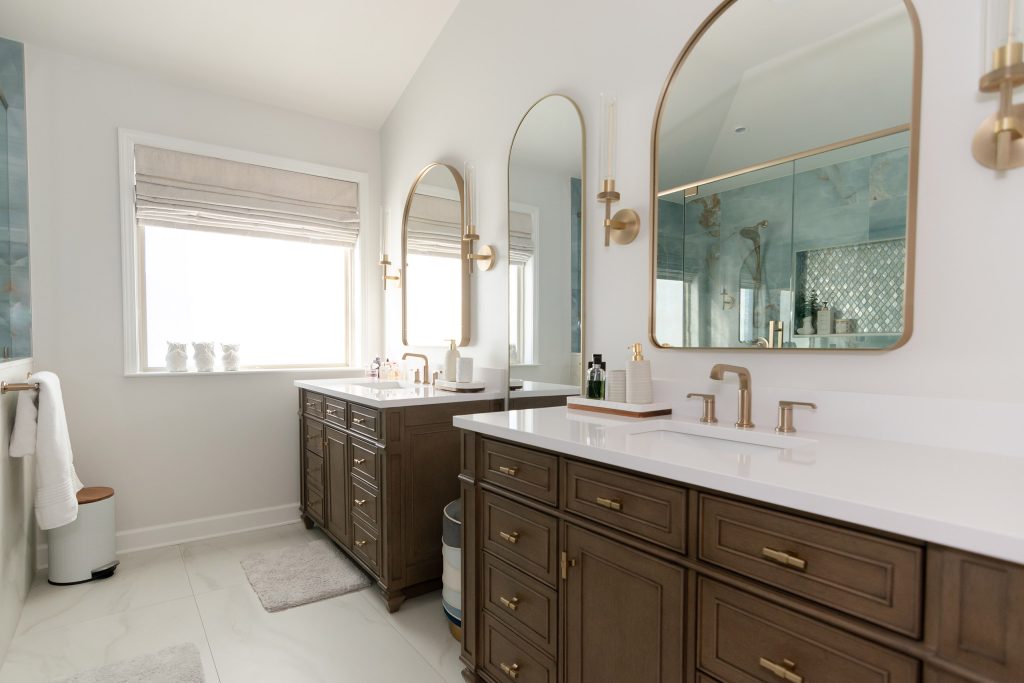 Master bath with a bright window, two dark-wood vanities with white quartz, and an arched mirror reflecting the onyx shower.