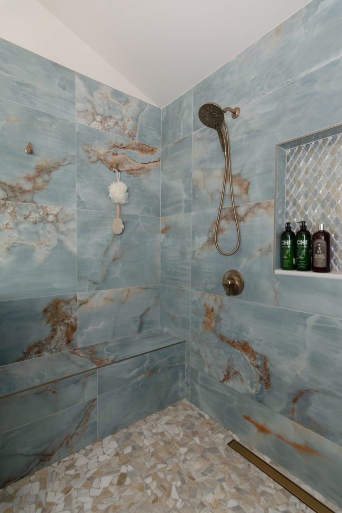Corner of the blue onyx shower with a diamond mosaic niche, a floating bench, and a pebble floor under a vaulted ceiling.