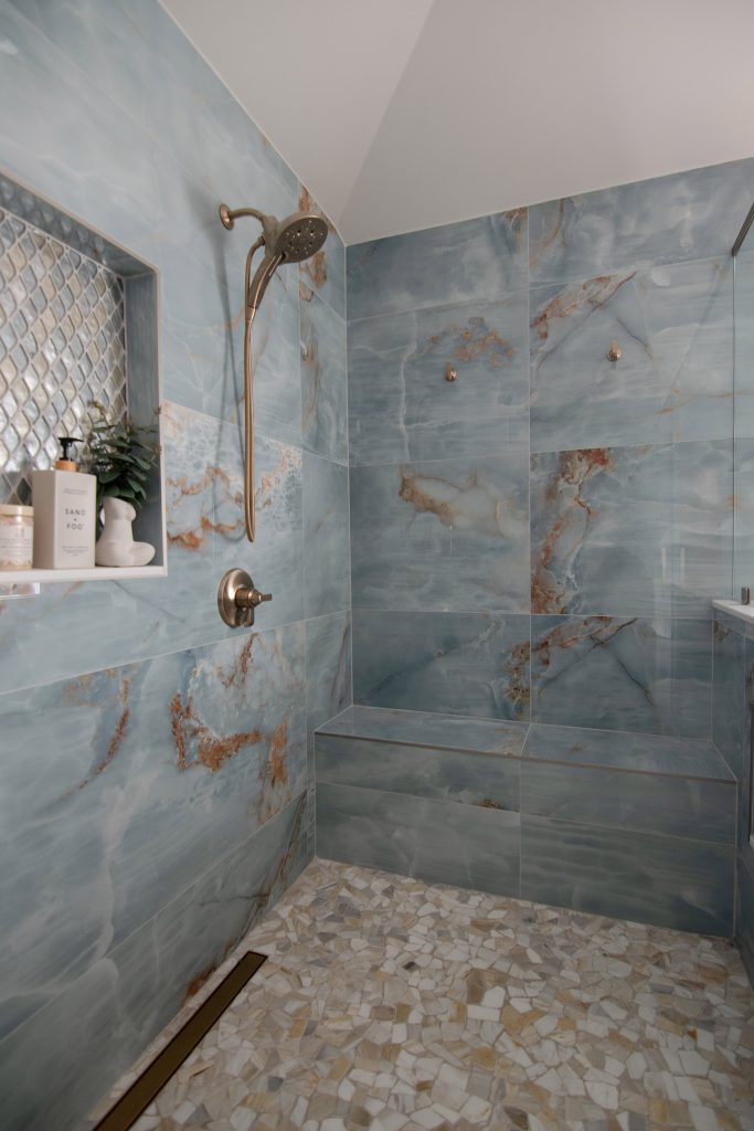 Blue onyx shower with a diamond mosaic niche, a long bench, and a pebble floor, glass half-wall and door to the left.