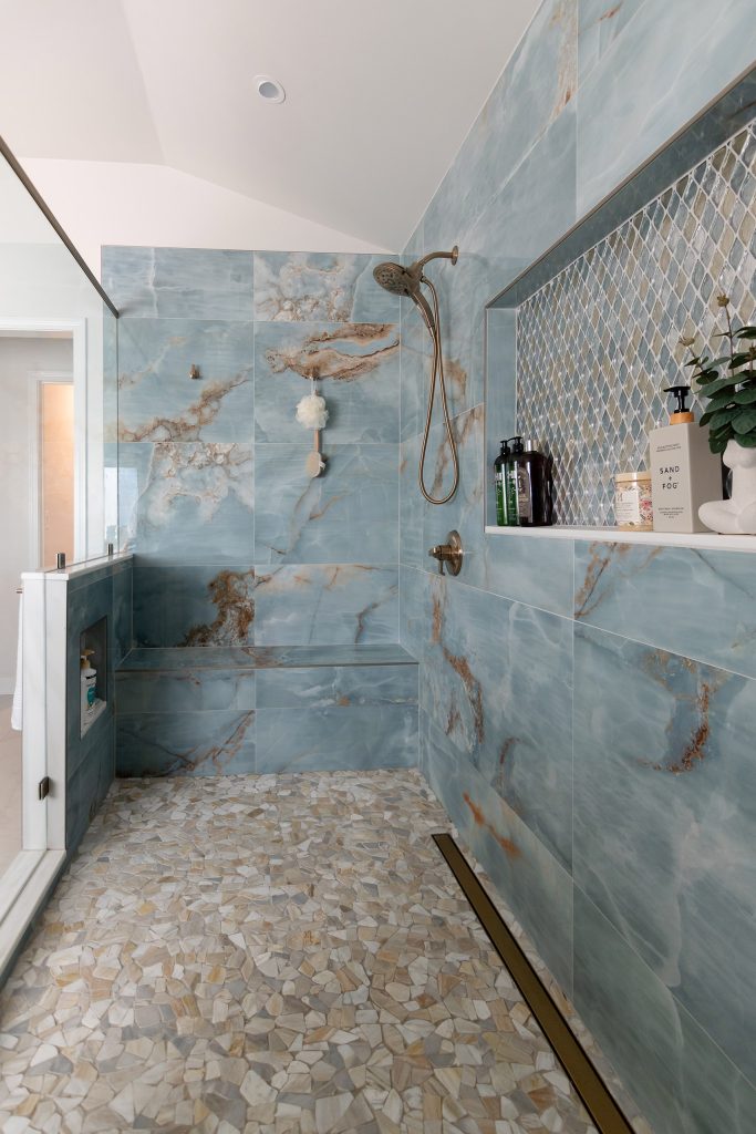 Blue onyx shower with a diamond mosaic niche, a long tiled bench, and a pebble floor, with a glass wall on the left.
