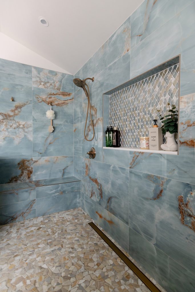 Vertical view of the blue onyx shower with a diamond mosaic niche, a long bench, and a river-pebble floor under a vaulted ceiling.