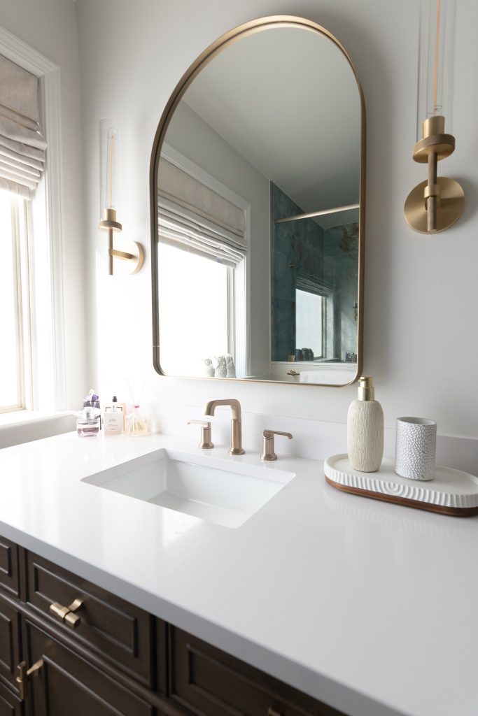 Close view of a dark-wood vanity with white quartz counter, undermount sink, and a champagne-bronze widespread faucet.