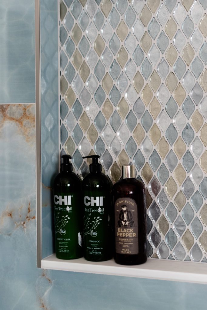 Shower niche detail with a shimmering teardrop glass mosaic backdrop and dark shampoo bottles against blue onyx tile.