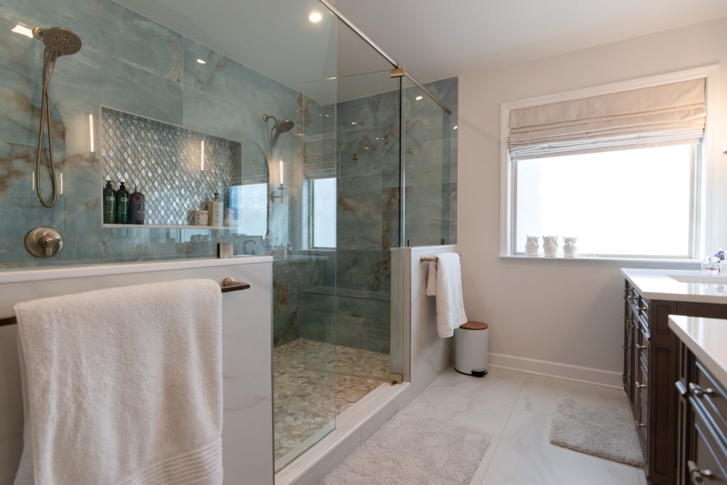 Glass-enclosed blue onyx shower with a diamond mosaic niche and bench, next to a window and marble-look flooring.