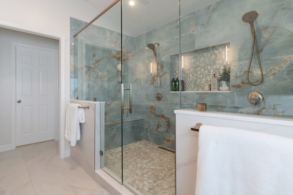Walk-in shower clad in blue onyx stone with amber veining, dual shower heads, a diamond mosaic niche, and a pebble mosaic floor.