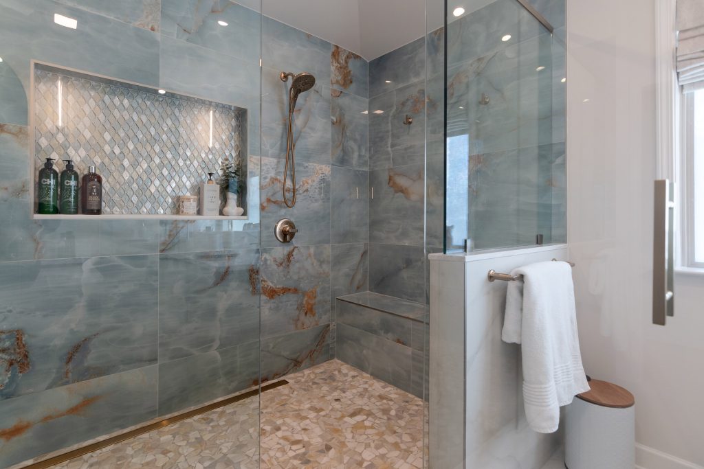 Blue onyx shower interior with a diamond glass-mosaic niche, a tiled bench, brushed-nickel heads, and a pebble mosaic floor.