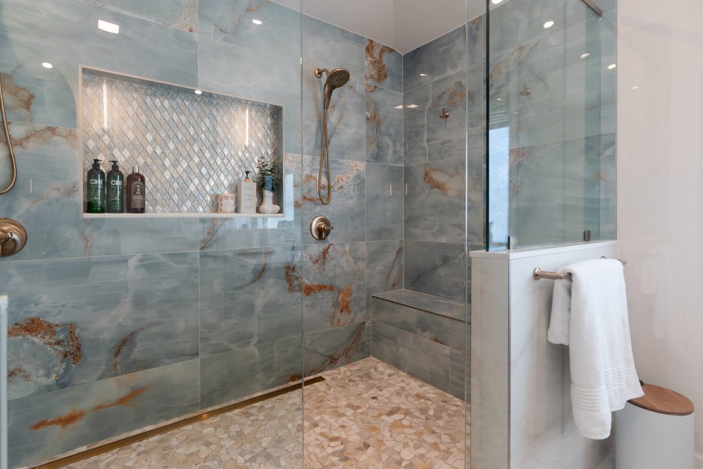 Blue onyx shower interior with a lit diamond mosaic niche, a floating bench, and a warm pebble mosaic floor.