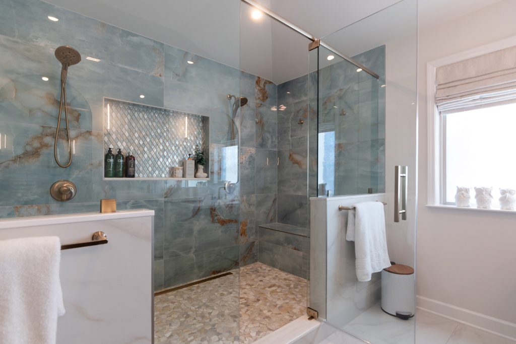 Blue onyx shower seen from the bath, with a diamond mosaic niche, dual heads, a bench, and a river-pebble floor.