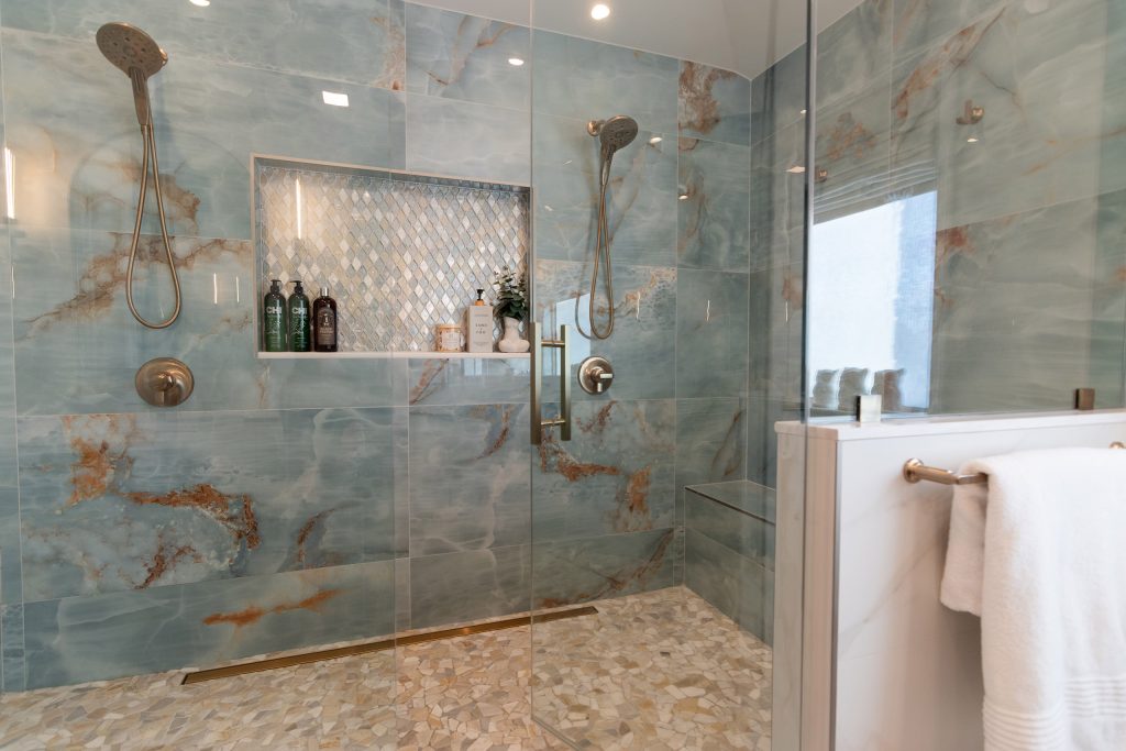 Walk-in shower clad in blue onyx stone with amber veining, a diamond mosaic niche, and a pebble mosaic floor.