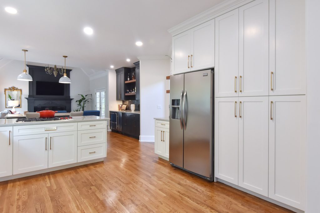 Alpharetta kitchen with floor-to-ceiling white pantry cabinets, a stainless refrigerator, oak floors, and a navy bar beyond.