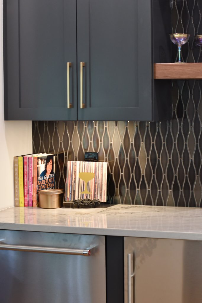 Navy bar cabinet with gold pulls, cookbooks, and a copper canister against iridescent tile above a veined marble counter in Alpharetta.