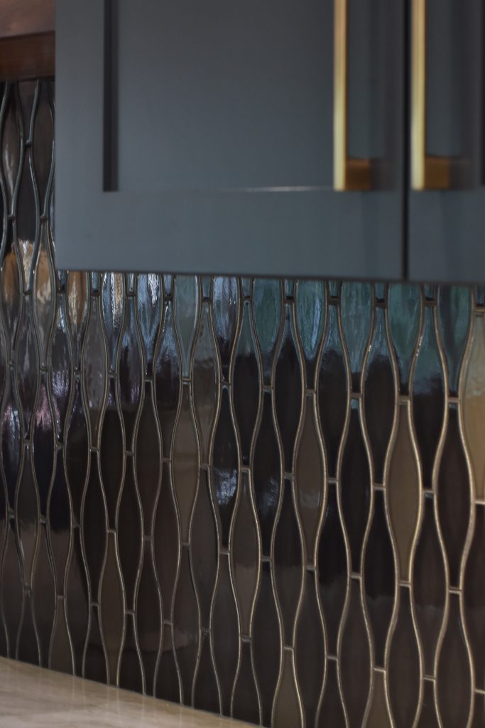 Macro of iridescent elongated-hexagon glass backsplash tile beside a navy cabinet with gold hardware in Alpharetta.