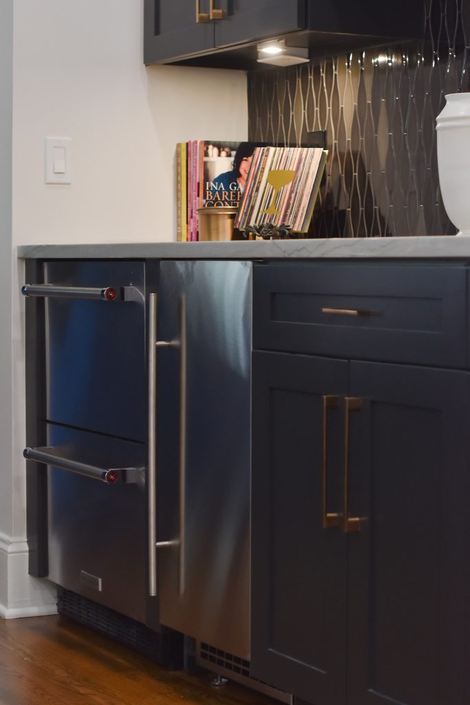 Navy bar cabinet detail with stainless beverage drawers, a stainless bar fridge, cookbooks, and iridescent tile in Alpharetta.