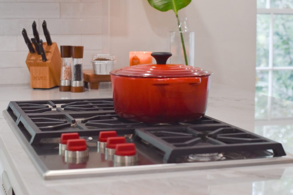 Stainless gas cooktop with a red Dutch oven, knife block, and salt-and-pepper mills on a marble-look counter in Alpharetta.