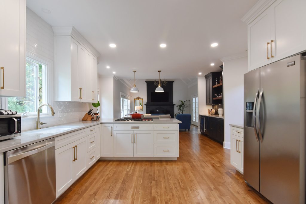 Open Alpharetta kitchen with white cabinets, stainless dishwasher and refrigerator, oak floors, and a navy bar in the background.