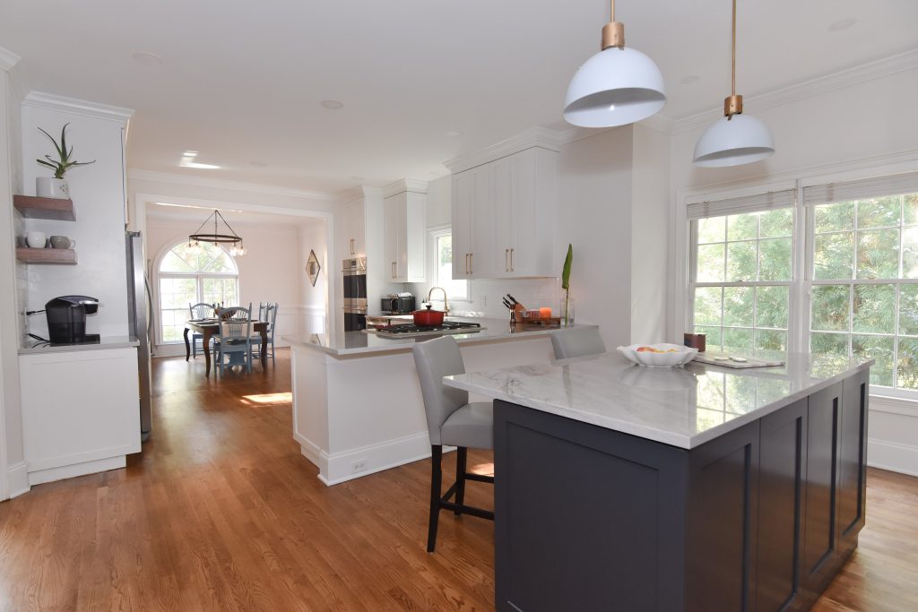 Navy island with veined marble top and gray stools under gray pendants, with a breakfast area and arched window in Alpharetta.