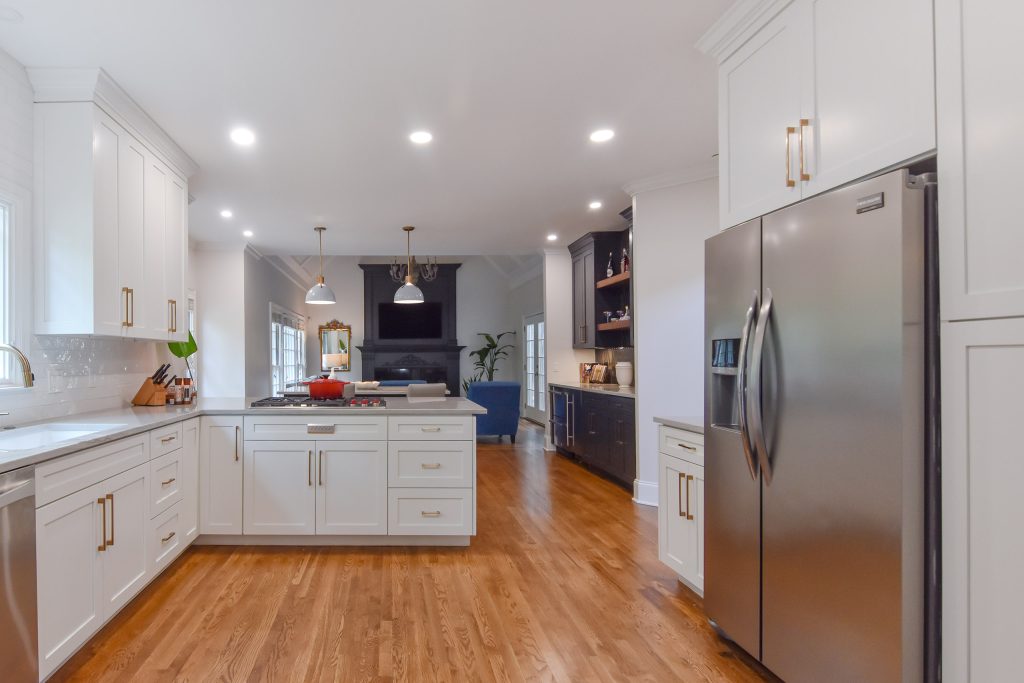 White Alpharetta kitchen with a window over the sink, brushed-gold hardware, peninsula, and a living room with a dark fireplace beyond.