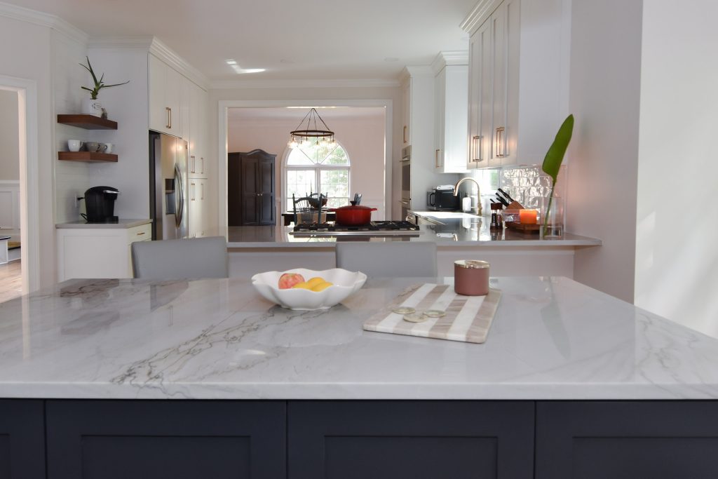 Veined marble island top with a fruit bowl and board, opening to the coffee nook and peninsula in an Alpharetta kitchen.