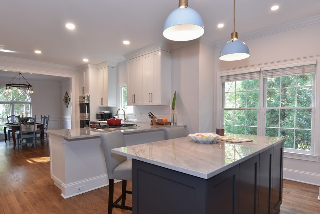 Navy island with a veined marble top and gray stools under gray dome pendants, beside a breakfast area with an arched window in Alpharetta.