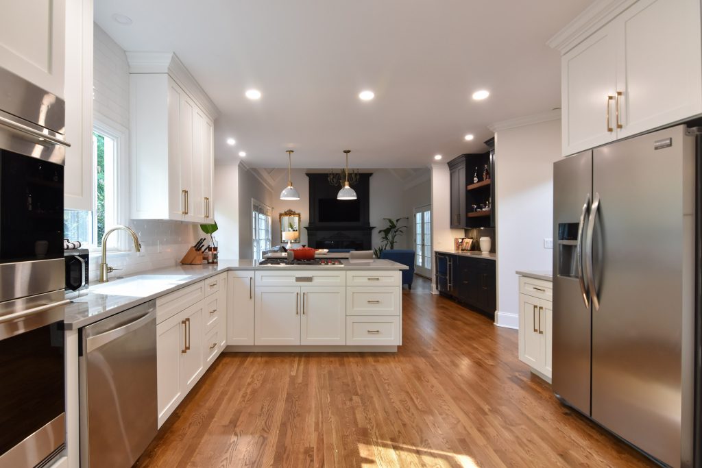 White Alpharetta kitchen with wall ovens at left, a sink under the window, peninsula, and a living room with a navy fireplace beyond.