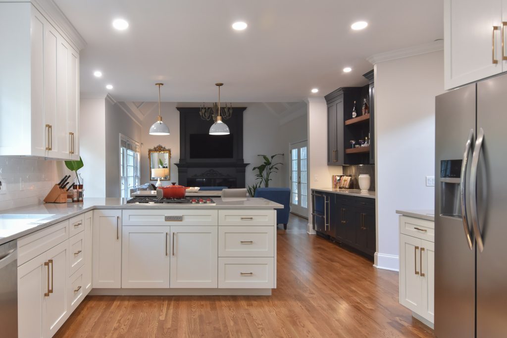 White Alpharetta kitchen with peninsula cooktop, oak floors, and a living room with a dark fireplace, with the navy bar at right.