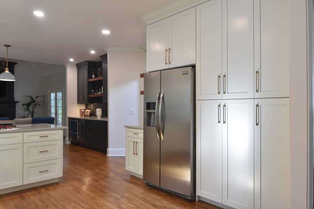 Open Alpharetta kitchen with a white island cooktop, oak floors, gray pendants, and a dark living-room fireplace in the distance.