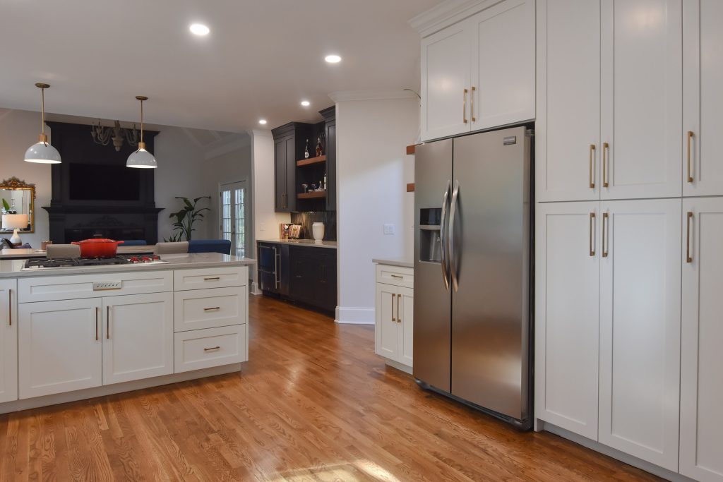 Stainless refrigerator between tall white pantry cabinets, with a navy bar and oak floors in an open Alpharetta kitchen.
