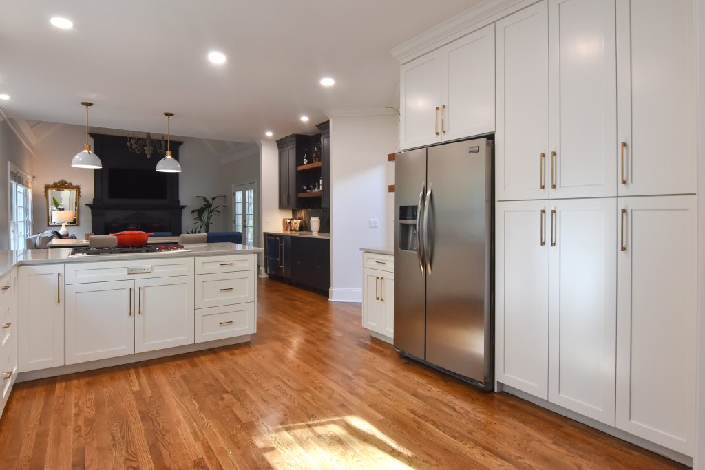 White Alpharetta kitchen with tall pantry cabinets, stainless refrigerator, oak floors, and a navy bar in the far corner.